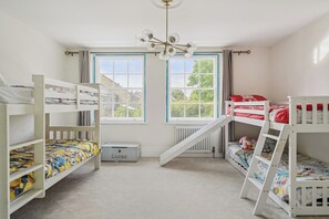 Een kinderkamer met stapelbedden, een kledingkast en een raam met uitzicht op huizen.
