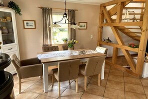 Ein Essbereich mit einem Holztisch, vier Stühlen, einer Chandelierleuchtre und einer Holzregaleinrichtung mit Dekorationsobjekten.