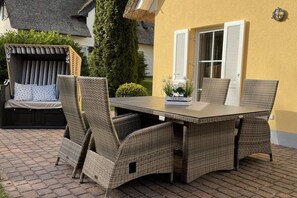 Ein Essbereich im Freien mit Korbmöbeln und einem Tisch, umgeben von einer Ziegelterrasse und einer gelben Wand.