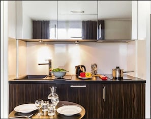 Cocina moderna con encimera de madera oscura, un lavamanos y una zona de comedor con platos y vasos.