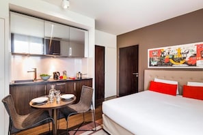Habitación de hotel con cama, una mesa de comedor con sillas, kitchenette y un cuadro abstracto grande en la pared.
