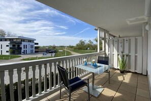 A balcony with a table and chairs, overlooking a building and a road. - Harbor idyll holiday apartment steering wheel (Karlshagen)