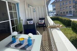 A balcony with two chairs, a table with a vase and a candle, and a view of a building. - Harbor idyll holiday apartment steering wheel (Karlshagen)