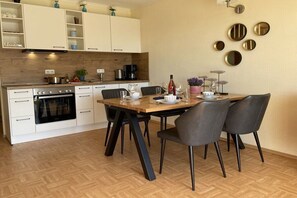 A modern kitchen with white cabinets, a wooden countertop, and a dining area with a table and chairs. - Harbor idyll holiday apartment steering wheel (Karlshagen)