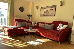 Un sofá rojo con una mesita de centro redonda, un reloj de pared, un cuadro enmarcado y una lámpara de pie.