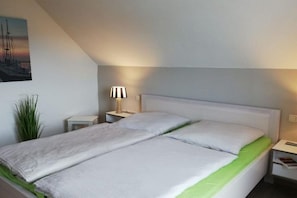 A single-bed room with a sloped ceiling, a bedside lamp, a small bedside table, and a green bedspread. - Holiday home with 1 bedroom (Poel \/ OT Kaltenhof)