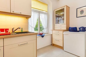 Cuina amb un rentaplat, armaris, una finestra amb cortines i un frigorífic.