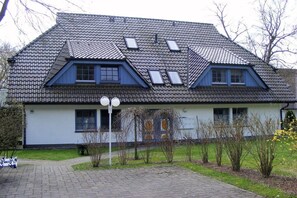 Ein Haus mit einem steilen Satteldach, Dachgauben und einem kleinen Vorgarten mit einem gepflasterten Weg.