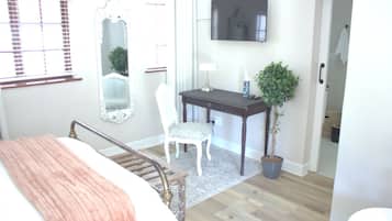 A bedroom with a bed, a desk, a chair, a TV, and a potted plant.