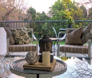 A balcony with two cushioned chairs, a small table with a decorative item, and a potted plant.