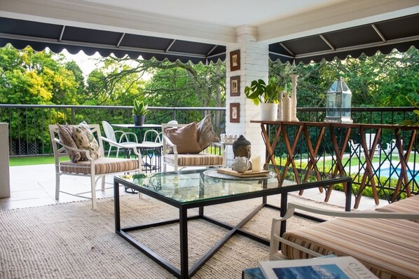 An outdoor patio with a glass-top table, white chairs, and a view of a pool.