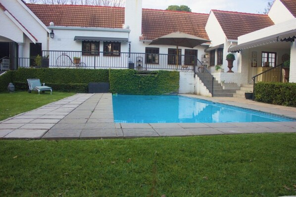 A residential property with a swimming pool, a covered patio, and a staircase leading to the entrance.