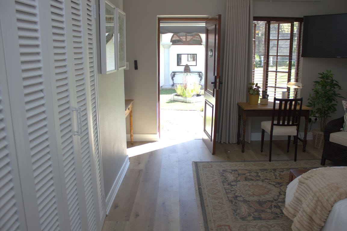 Una habitación con cama, un escritorio con silla, una planta en maceta y vista al exterior.