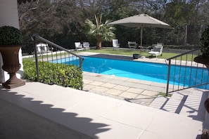 A swimming pool with a metal railing, surrounded by potted plants and outdoor chairs.