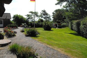 Un sentier de jardin menant à un bâtiment surmonté d’un mât porte-drapeau.