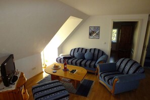 Un salon comprenant un canapé, un fauteuil, une table basse et un téléviseur posé sur un meuble en bois.