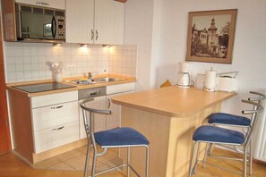 A compact kitchen with white cabinets, a microwave, a sink, and a small island with bar stools. - 02 Heringsdorf Lake Castle (Heringsdorf)