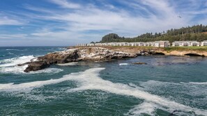 A coastal hotel with a rocky shoreline, ocean waves, and a forested hill in the background. - Oregon Coast 2BR Queen at WorldMark Depoe Bay – Stunning Views (Depoe Bay)
