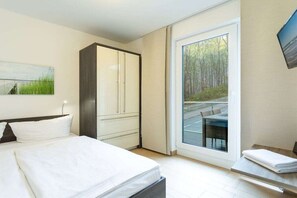 A hotel room with a bed, a wardrobe, a sliding glass door to a balcony, and a painting on the wall. - 8 in the Capitello Residence (Ostseebad Binz)