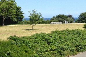 A grassy park area with a bench and a statue, trees, and a view of the sea. - Holiday apartment with 2 bedrooms (Hohwacht)
