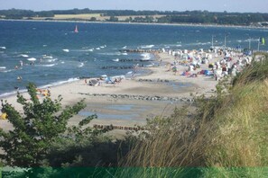 Ein Strand mit Zelten und Menschen, ein sandiger Uferstreifen und ein Gewässer.