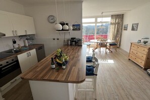 Eine moderne Küche mit einer Holztischinsel, einem Essbereich mit Tisch und Stühlen sowie Blick ins Freie durch große Fenster.