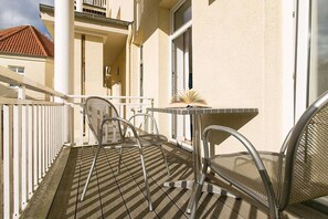 A balcony with a table and two chairs, a white railing, and a building in the background. - Holiday apartment in Binz with swimming pool (Binz)