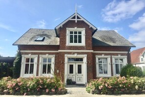 Ein zweistöckiges Haus mit einer symmetrischen Fassade, einem zentralen Eingang mit Doppeltüren und einem kleinen Giebelzimmer im Dach.