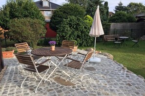 Eine Terrasse im Freien mit einem Steintisch, vier Stühlen, einer Bank und einem großen Sonnenschirm.