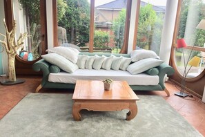A cozy room with a green sofa, a wooden coffee table, and a view of a garden through large windows. - Wyk's Captain's House (Wyk auf Föhr)