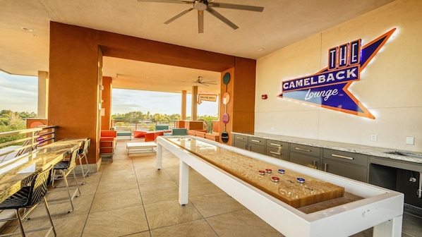 A camelback lounge with a shuffleboard table, seating area, and a view of the outdoors. - Scottsdale Studio Hotel at WorldMark – Pools, Golf & Desert Views (Scottsdale)