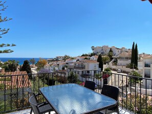 A balcony with a glass table and chairs, overlooking a coastal town with terracotta roofs and white buildings. - Villa in Nerja Near Burriana Beach (Nerja)