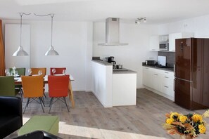 A modern kitchen with white cabinetry, a dark refrigerator, and a dining area with colorful chairs. - Apartment in Plau am See with swimming pool (Plau am See)