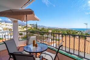 A balcony with a table and chairs, an umbrella, and a view of a coastal town and mountains. - Two-bedroom Villa Near the Beach (Nerja)