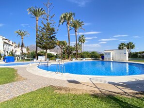 A swimming pool with a tiled deck, surrounded by palm trees and a clear sky. - Two-bedroom Villa Near the Beach (Nerja)