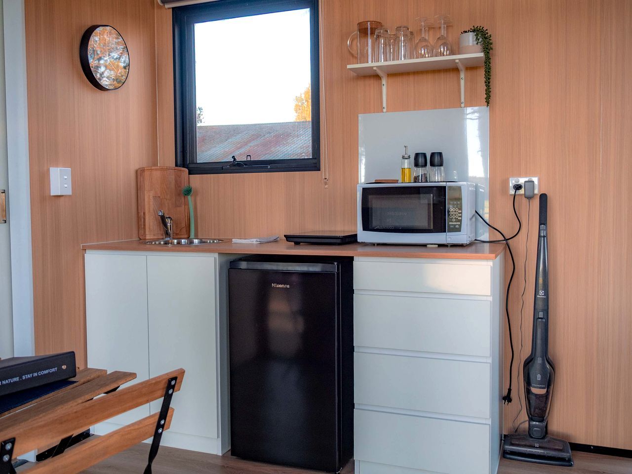 Una cocina compacta con microondas, un refrigerador pequeño y una aspiradora.