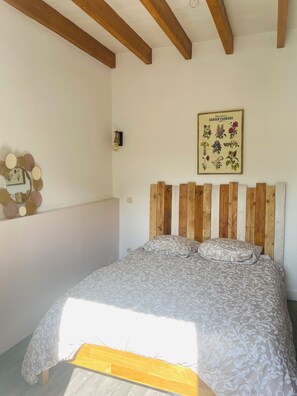Ein Schlafzimmer mit einem hölzernen Kopfteil, einem Bett mit gemusterten Betttextilien, einer wandmontierten Leuchte und einem gerahmten Pflanzenbild.