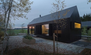 A modern house with a sloped roof, large windows, and a stone pathway leading to a bench.
