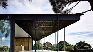 Un edificio moderno con fachada de vidrio amplia, interior de madera y estructura de techo metálica.