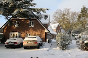 A two-story brick house with a snow-covered driveway and parked cars. - Holiday home with 2 bedrooms (Wyk auf Föhr)