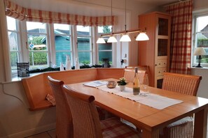 A dining area with a wooden table, wicker chairs, and a view of the outside through large windows. - Holiday home with 2 bedrooms (Wyk auf Föhr)