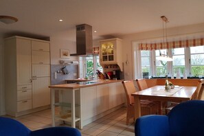 Una cocina con armarios blancos, una isla central y una zona de comedor con sillas azules.