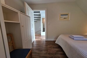 Un dormitorio con cama, una silla, un armario y una escalera que lleva a otra habitación.