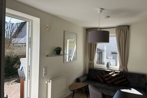 A living room with a sofa, a small table, a hanging light fixture, and a window with curtains. - Holiday apartment with 1 bedroom (Ostseebad Baabe)