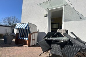 An outdoor seating area with a glass door leading to a room, a wicker chair with a striped cushion, and a table with chairs. - Holiday apartment with 1 bedroom (Ostseebad Baabe)