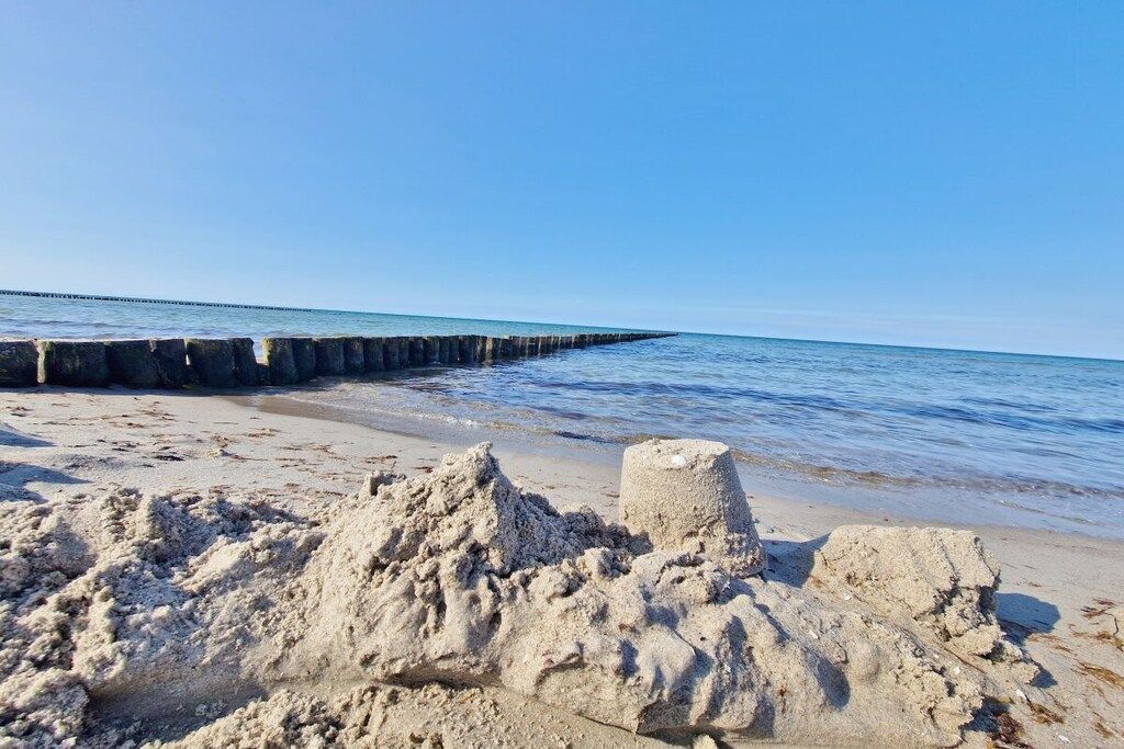 Une plage de sable avec une digue en béton qui s’avance dans l’eau.
