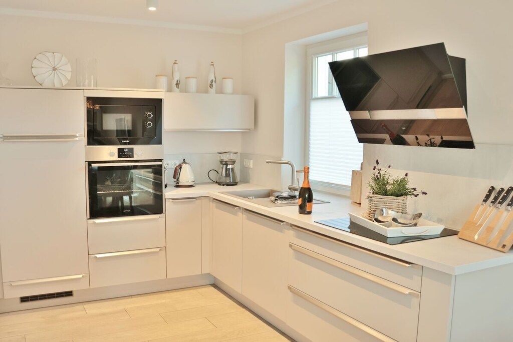 A modern kitchen with built-in appliances, a large window, and a flat-screen TV mounted on the wall.