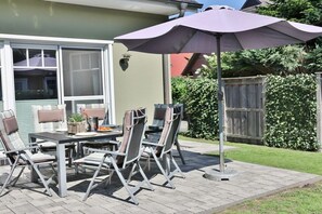An outdoor patio with a table and chairs, a purple umbrella, and a wooden fence in the background. - Holiday home in Zingst with swimming pool (Zingst)