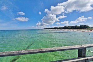 A beach with clear water, a wooden pier, and a distant shoreline with trees. - Holiday home in Zingst with swimming pool (Zingst)