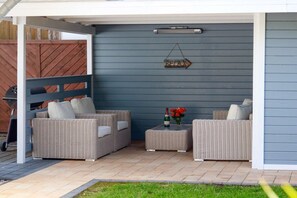 An outdoor patio area with wicker furniture and a small table with a bottle and flowers. - Holiday home in Zingst with Wi-Fi and parking (Zingst)